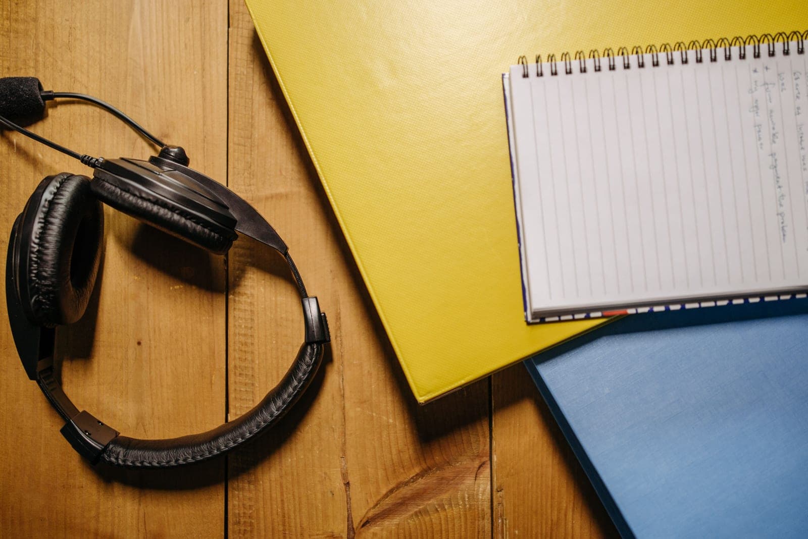 Flat lay of black headphones, a notebook and folders on a wooden surface