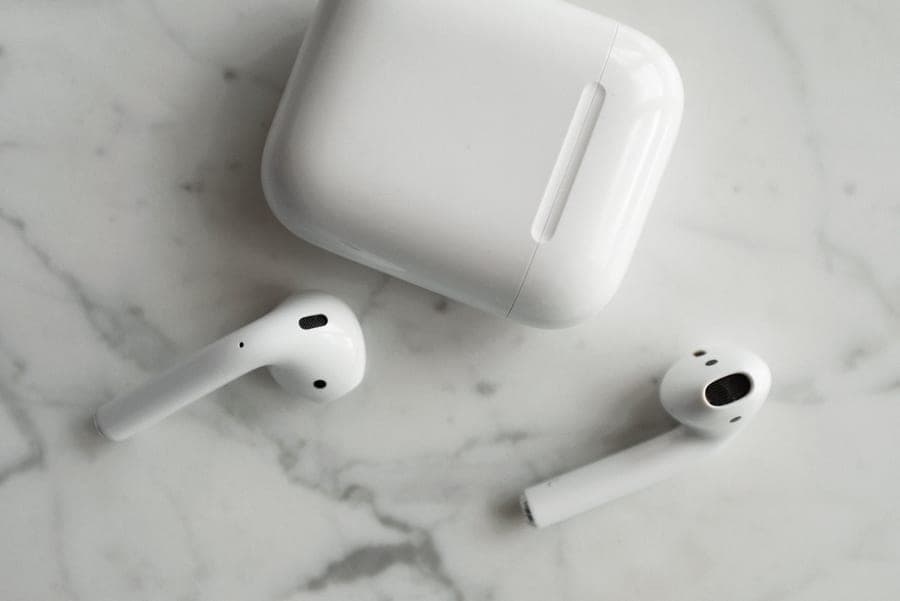 White wireless earbuds beside a charging case on a pale surface